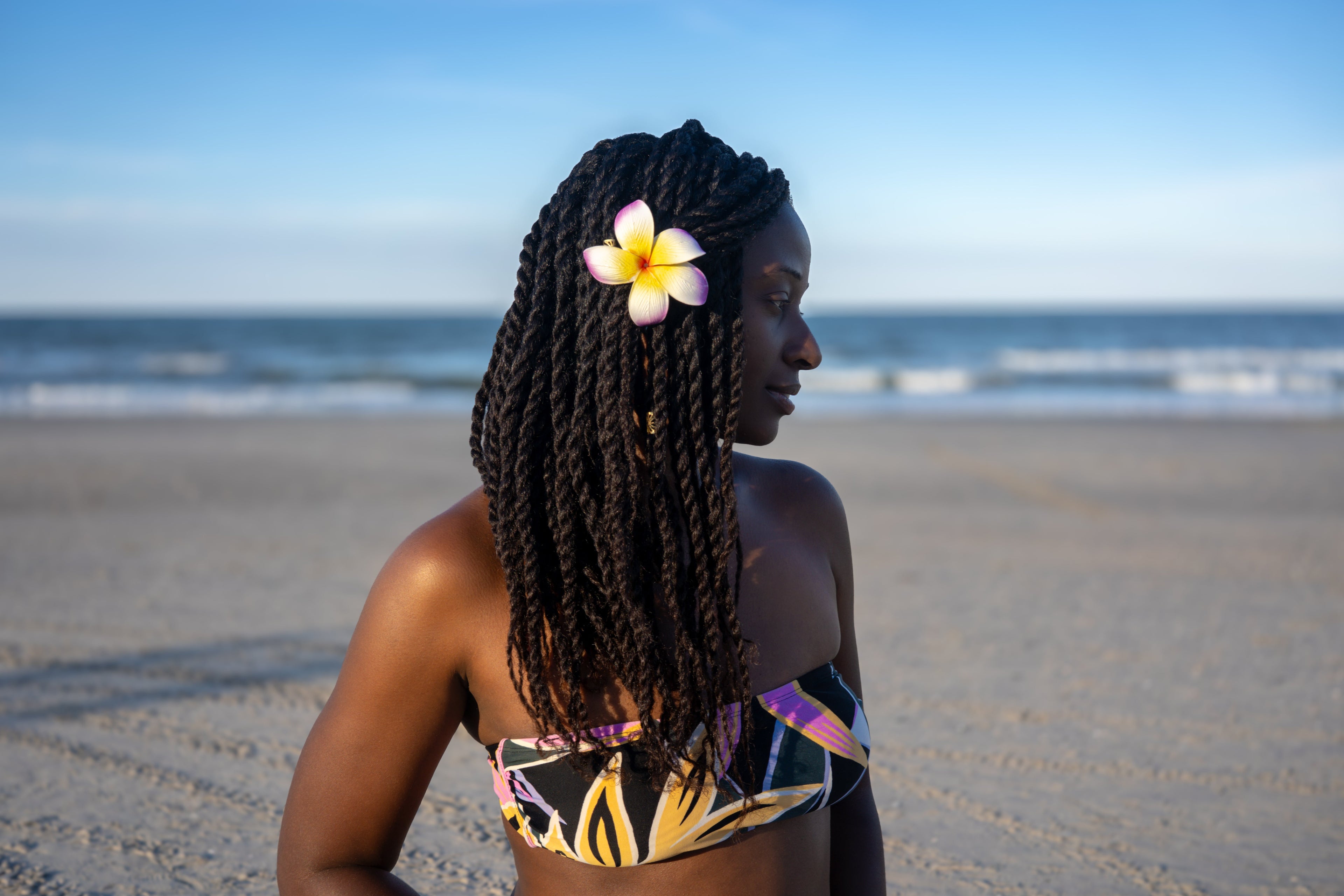 Woman with braided hair and a flower in her hair standing on a beach.