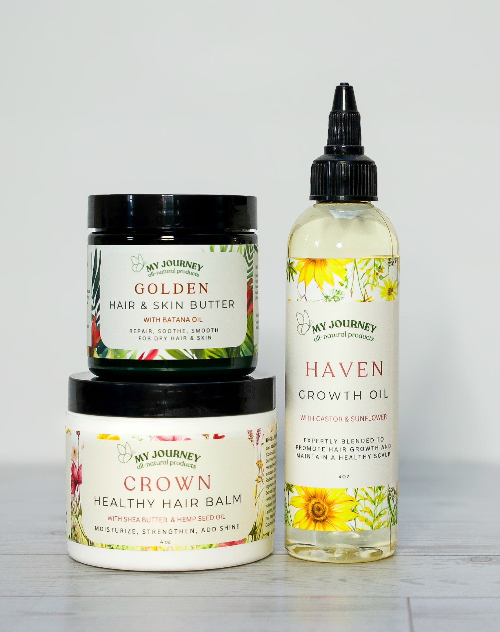 Three hair care products from My Journey Organics arranged on a light gray surface against a white background: a jar of Golden Hair & Skin Butter, a container of Healthy Hair Balm, and a bottle of Haven Growth Oil.